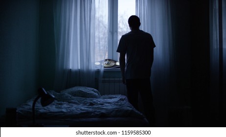 Alone man silhouette staring at the window closed with curtains in bedroom. Man stands at window alone - Shutterstock ID 1159585300