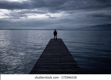 Alone Man Standing On The Edge Of A Pier In Twilight