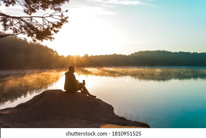 Alone Man Stands On The Peak Of Rock In National Park And Watching To Sun Rise. Beautiful Moment The Miracle Of Nature. Misty Lake. Man Hike. Person Silhouette Sit. Foggy Mountains. Relax. Calm.