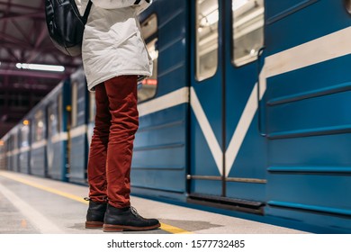 Alone man waiting while subway train open the door. Well-dressed handsome male in black boots and red trousers with black backpack on his back stay on station platform. Public transport concept.