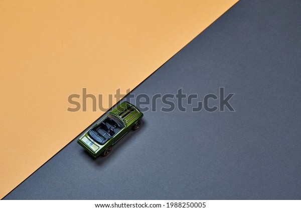 Alone micro toy\
small mini model car top view isolated on the asphalt road color\
fond background with diagonaly oriented beige-orange-yellow paper\
background