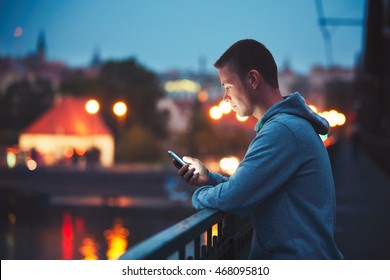 Alone in the night city with mobile phone. Handsome dreamy man reading message (or looking on the video) on his smartphone. - Powered by Shutterstock