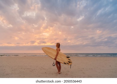 Alone surfer woman on beach with warm sunset tones. Attractive surf girl with surfboard