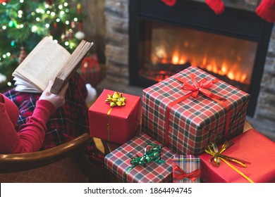 Alone Woman Covered Plaid Reading Book Sitting And Relaxation On Armchair Near Fareplace And Christmas Tree After Finishing Pakking Gift Boxes For Family. 