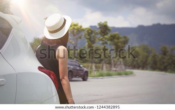 Alone Woman leaning back at hatchback car on road\
with mountain background. Female waiting technician fix car.\
Selective focus