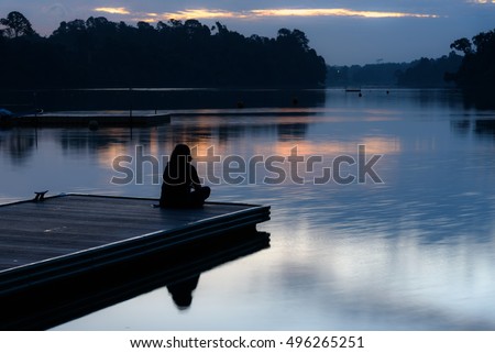 Alone women relax on wooden dock at peaceful lake, silhouette