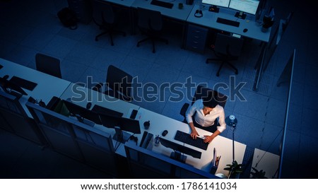Alone Working Late at Night in the Office: Businesswoman Using Desktop Computer, Analyzing, Using Documents, Solving Problems, Finishing Project. High Angle Shot