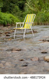 Alone yellow chair put in stream rocky waterfall with green environment forest nature background.