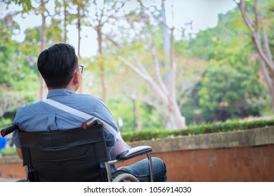 Alone Young Disabled Man On Wheelchair In The Park, Patient Is Relaxing In Garden Decorations Of The Hospital Feeling Of Missing Someone, Lonely