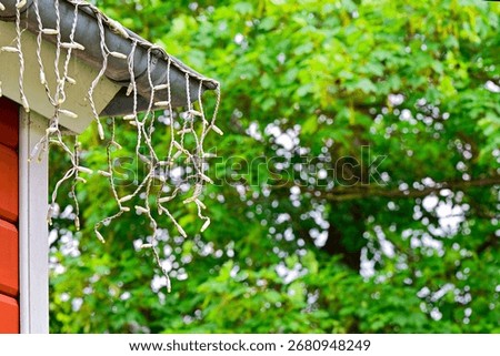 Along the eaves a cable carries warm string lights with short hanging drops. A metal downspout anchors the corner, creating a cozy exterior mood for home decor and evening lifestyle visuals.