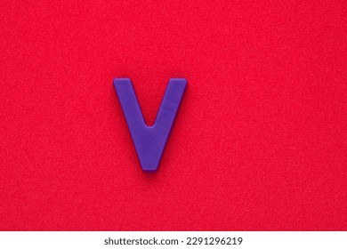 Alphabet letter V - Violet colored plastic piece on red 032 c foamy background