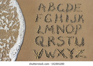 Alphabet letters handwritten in sand on beach