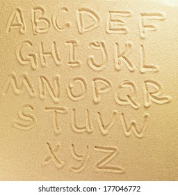 Alphabet letters handwritten in the sand on the beach