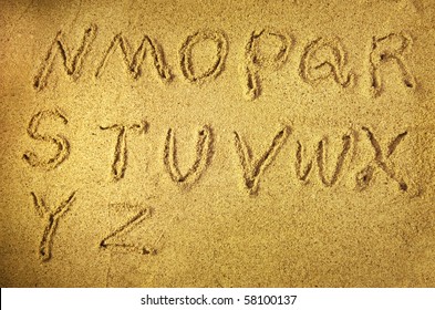 alphabet letters handwritten in sand on beach