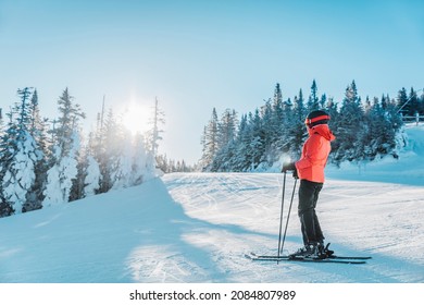 Alpine Downhill Skiing. Ski portrait of woman alpine skier wearing skis, helmet, cool ski goggles and hardshell winter jacket and ski gloves on cold day by snow covered trees on ski trail slope.
