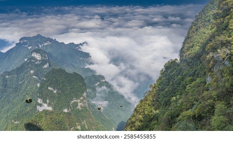 Alpine  funicular. Cable-stayed cabins of cableway above the gorge. Green vegetation on the mountain slopes. The peaks in the clouds. Blue sky. China. Tianmen Mountain