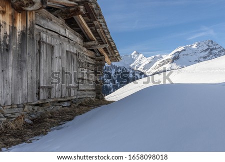 Alpine hut and mountain range covered in snow. Mountain peaks in background Piz Tambo and Guggernüll