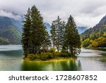 Alpine lake Di Predil in the fog. Small island in the middle of the lake is overgrown with pine trees. Among the pines there is a red tourist tent. The concept of mountain  and photo tourism