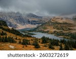 Alpine lake surrounded by dramatic mountain cliffs and low-hanging clouds in Glacier National Park
