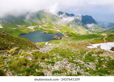 alpine landscape of fagaras mountains. balea lake of romania in summer. cloudy weather in dappled light. spots of snow and grass on the rocky hillsides of carpathian range