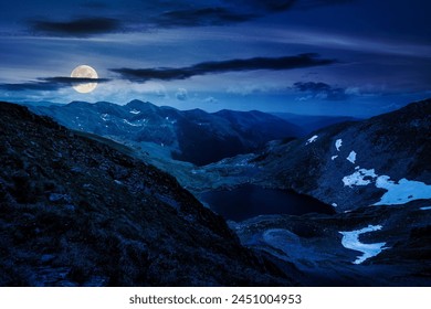 alpine landscape of fagaras mountains at night. capra lake of romania in summer. spots of snow and grass on the rocky hillside in full moon light. stunning travel destination - Powered by Shutterstock