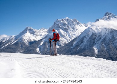 Alpine mountain panorama in winter.  Hiker with a backpack and poles on a prepared winter hiking trail looks at the Swiss Alpine chain.  Snow-capped mountain peaks and white clouds against a blue sky - Powered by Shutterstock