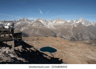 Alpine observatory in Gornergrat Switzerland near Zermatt overlooking an alpine lake, trails, and the snow capped mountains under a blue sky - Powered by Shutterstock