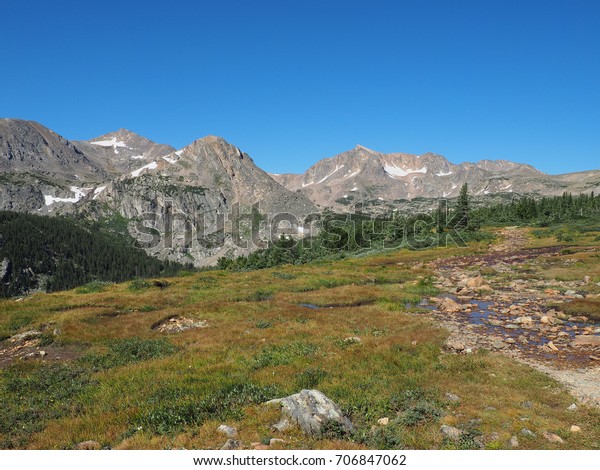 Alpine trail leading\
towards mountain peaks on clear summer day in Indian Peaks\
Wilderness in Colorado 