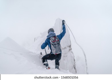 An Alpinist Climbing An Alpine Ridge In Winter Extreme Conditions. Adventure Ascent Of Alpine Peak In Snow And On Rocks. Climber Ascent To The Summit. Winter Ice And Snow Climbing In Mountains.