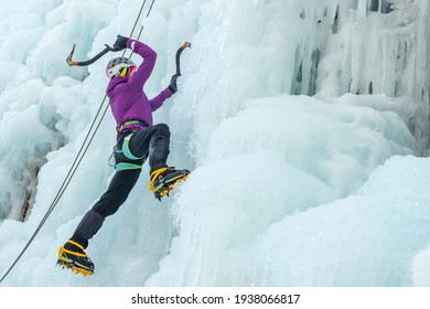 Alpinist woman with ice climbing equipment, axe and climbing ropes, hiking at a frozen waterfall