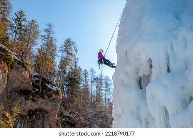 Alpinist Woman With Ice Climbing Equipment On A Frozen Waterfall