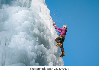 Alpinist Woman With Ice Climbing Equipment On A Frozen Waterfall