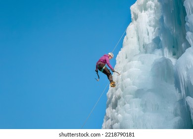 Alpinist Woman With Ice Climbing Equipment On A Frozen Waterfall