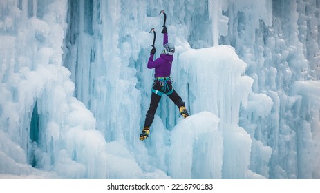 Alpinist Woman With Ice Climbing Equipment On A Frozen Waterfall