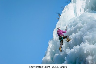 Alpinist Woman With Ice Climbing Equipment On A Frozen Waterfall