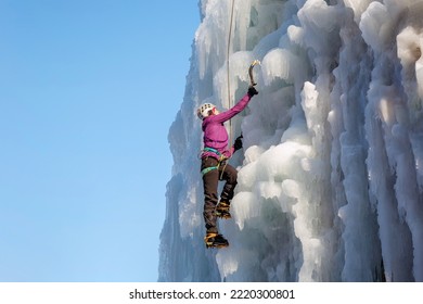 Alpinist Woman With Ice Climbing Equipment On A Frozen Waterfall