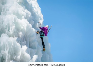 Alpinist Woman With Ice Climbing Equipment On A Frozen Waterfall