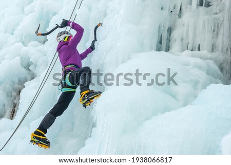 Alpinist woman with ice climbing equipment, axe and climbing ropes, hiking at a frozen waterfall