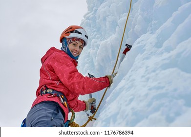 Alpinist woman with  ice tools axe in orange helmet climbing a large wall of ice. Outdoor Sports Portrait - Powered by Shutterstock