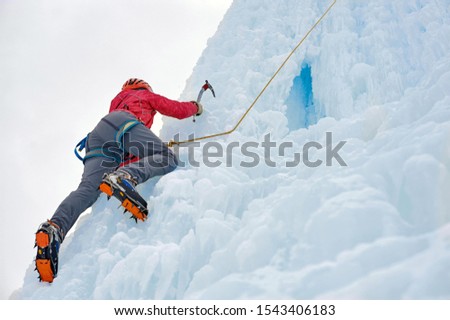Alpinist woman with ice tools axe in orange helmet climbing a large wall of ice. Outdoor Sports Portrait