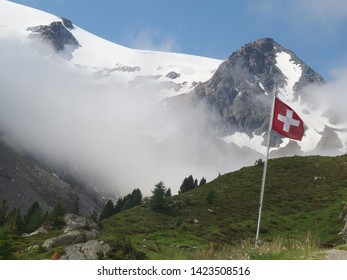 Alps, Switzerland, Tour du Mont Blanc - on the route from the Col de la Forclaz pass to the Col de Balme, view of snowy and cloudy mountains in sun and the Swiss flag on pole