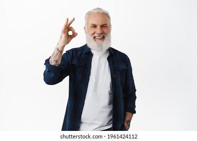 Alright. Handsome senior man laughing, showing okay OK sign and nod in approval, praise good work, making compliment, recommend good quality product, standing over white background - Shutterstock ID 1961424112