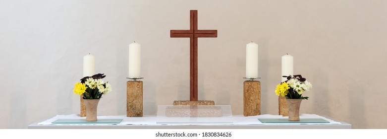 Altar with a wooden cross and four candles against a light background. Panorama
