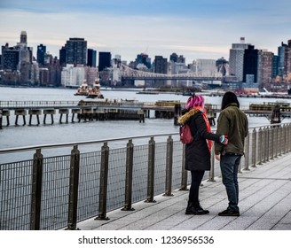 Alternative Artsy Young Couple In Love Holding Hands At The Riverside In Brooklyn New York With The City Skyline And The River In The Background