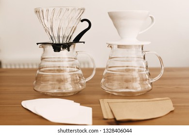 Alternative coffee brewing method. Stylish accessories and items for alternative coffee on wooden table. Glass flask with dropper, paper filters, glass and ceramic dripper for pour-over coffee - Shutterstock ID 1328406044