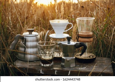 Alternative coffee brewing outdoors in travel. Steel kettle, hot coffee in cup, coffee dripper,  geyser maker, glass flask with filter on background of sunny warm light in rural herbs. - Powered by Shutterstock