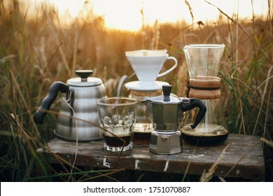 Alternative coffee brewing outdoors in travel. Steel kettle, hot coffee in cup, coffee dripper,  geyser maker, glass flask with filter on background of sunny warm light in rural herbs. - Powered by Shutterstock