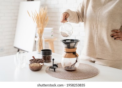 Alternative coffee brewing. Young woman brewing coffee in coffee pot standing at the white table with various stuff for alternative coffee brewing, pouring hot water into the filter - Shutterstock ID 1958253835