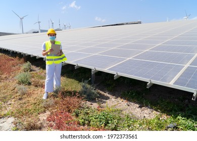 Alternative Energy Concept - Engineer Woman In Covid Mask During Pandemy Standing In Front Of Solar Panels, Green Energy And Eco Friedly Industry Concept