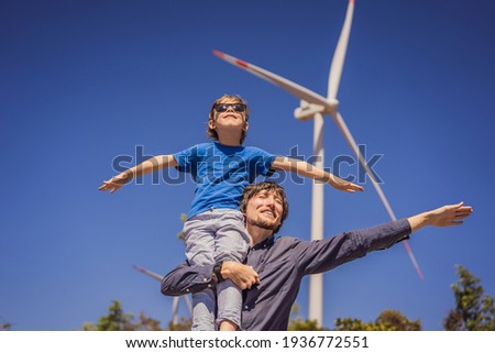 Alternative energy, wind farm and happy time with your family. Happy father carrying his son on shoulders is on vacation and escape to nature. Father carrying son on shoulders and waving their arms